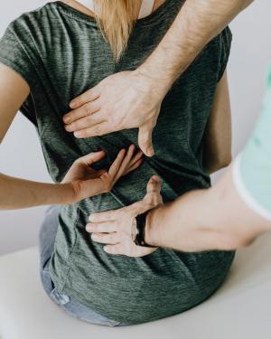 A doctor's hands touching a woman's back as she appears to be in pain 