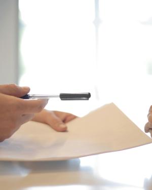 Hands holding paperwork across a negotiation table 