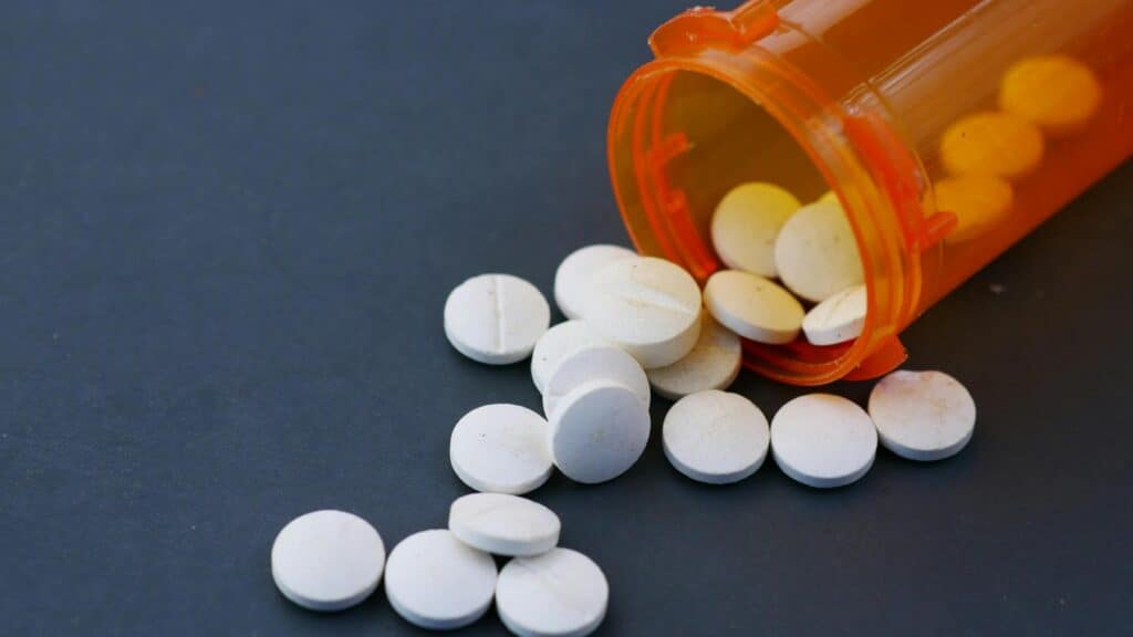 Prescription medication pills spilled from orange pill bottle on dark background.