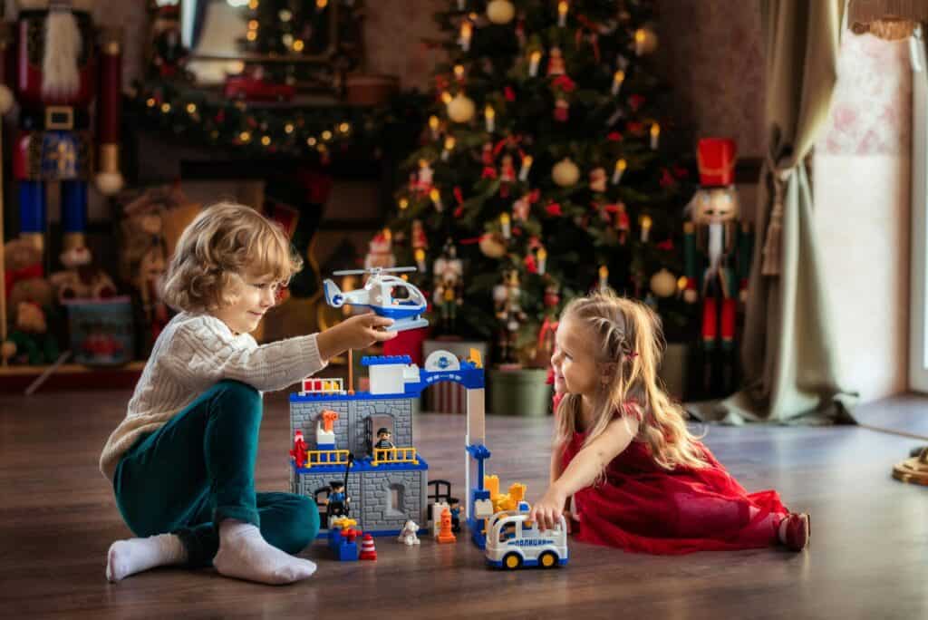 Children playing with toy police station and vehicles near Christmas tree.