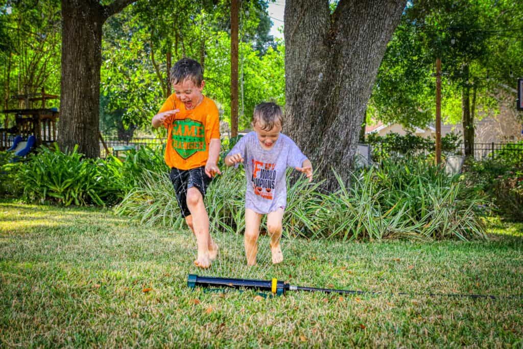 Kids enjoying summer fun with water sprinkler in a lush green yard.