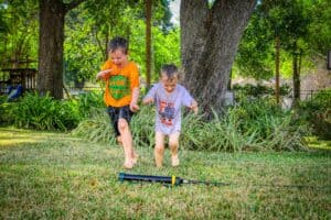 Kids enjoying summer fun with water sprinkler in a lush green yard.