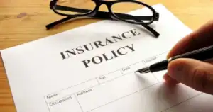 Person signing an insurance policy with glasses on a wooden table.