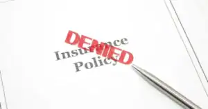 Insurance claim denied document with red stamped 'DENIED' and pen.